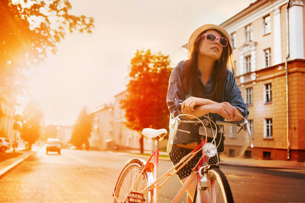 portrait of a beautiful young girl in a hat with a bicycle on city background in the sunlight outdoor - Φωτογραφία, εικόνα