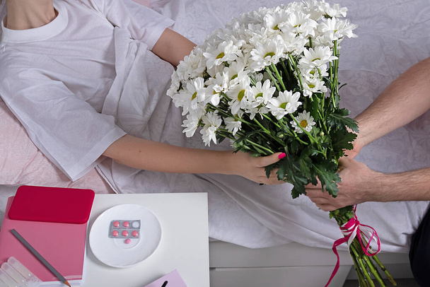 man gives flowers to sick girl. White chrysanthemums in male hands. Family care concept - Photo, image