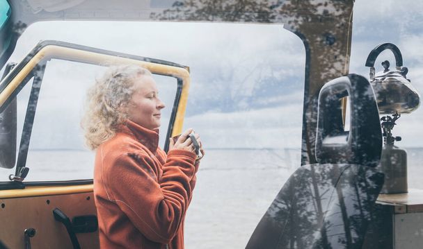 Junge blonde Frau neben Wohnmobil mit Blick auf das zugefrorene Wintermeer. Blick durch die offene Tür. - Foto, Bild