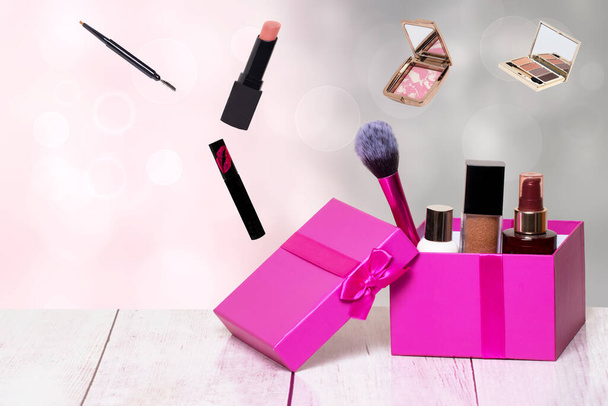 Díszítő összetétele színes szépség és smink termékek és eszközök egy rózsaszín ajándék doboz egy világos asztalon, és további kozmetikai tartozékok elvont háttérrel. Másolás helye a reklám a bal oldalon. - Fotó, kép