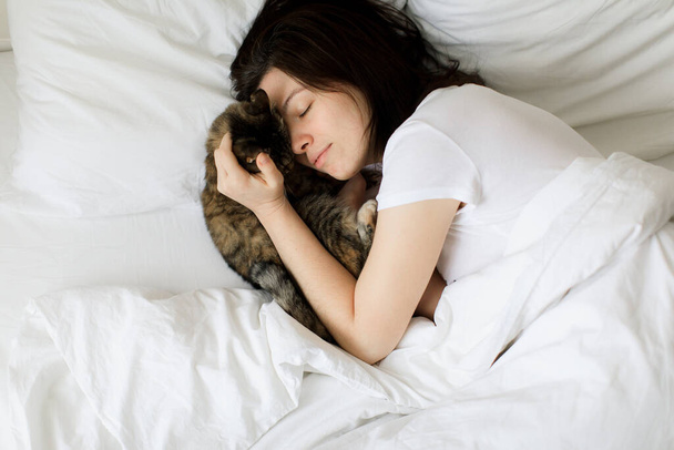 Mascotas, mañana, comodidad, descanso y concepto de personas - mujer joven feliz con gato en la cama en casa - Foto, Imagen