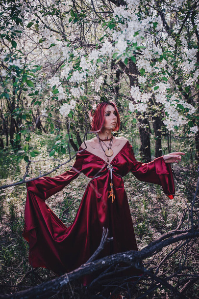 Girl in red and red hair in the form of a druid in apple trees - Фото, изображение