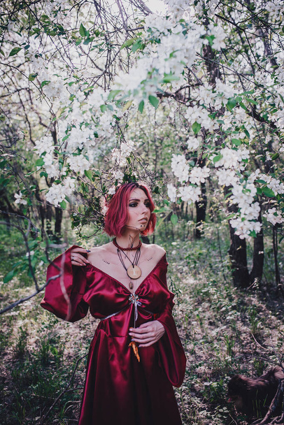 Girl in red and red hair in the form of a druid in apple trees - Fotó, kép