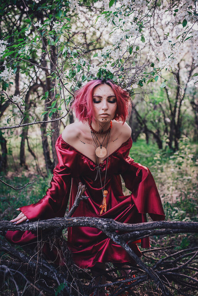 Girl in red and red hair in the form of a druid in apple trees - Foto, afbeelding