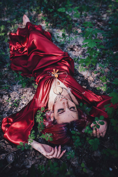 Chica de pelo rojo y rojo en forma de druida en los manzanos
 - Foto, imagen
