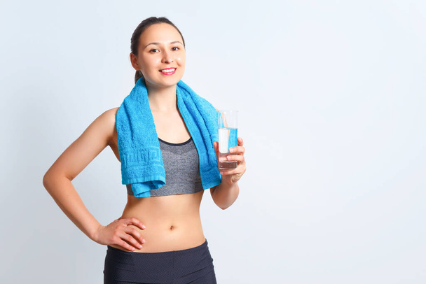 Portrait of a happy young fitness woman in sports clothes with a towel on her shoulders and glass of water on a blue background - Zdjęcie, obraz