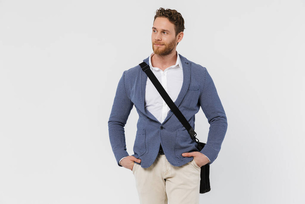 Image of handsome young man in jacket posing on camera with bag isolated over white background - Foto, immagini