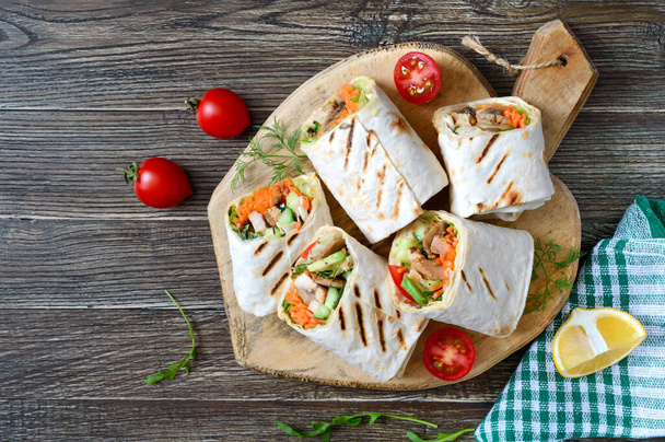 Fresh tortilla wraps with chicken, mushrooms and fresh vegetables on wooden board. Chicken Mexican burrito. Tasty appetizer. Dishes from pita bread. Healthy food concept. - Photo, Image