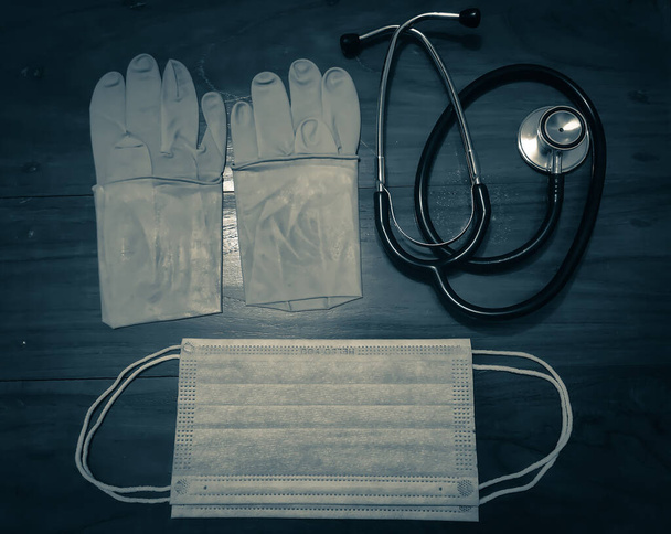 Para gumowych rękawic medycznych, maska chirurgiczna i czarny stetoskop na drewnianym stole. - Zdjęcie, obraz