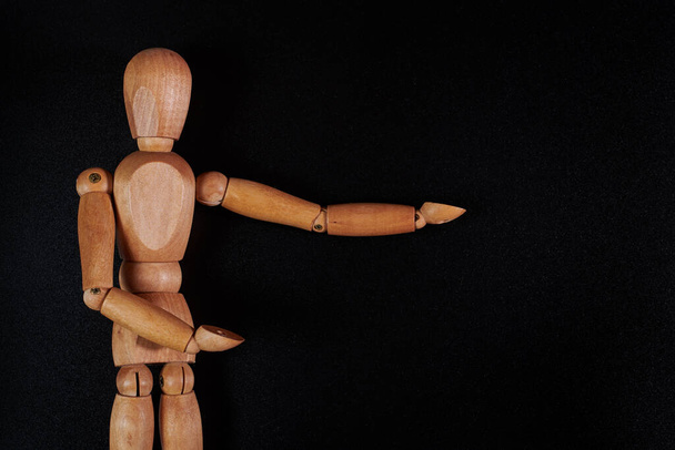 a wooden model of a man on a black background shows his wooden hands to the side. A puppet with wooden hands points to the side - Foto, afbeelding