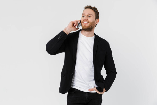 Image of handsome joyful man in jacket laughing and talking on smartphone isolated over white background - Fotografie, Obrázek