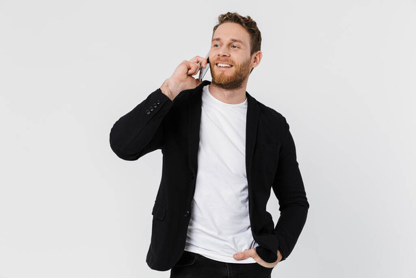Image of handsome joyful man in jacket laughing and talking on smartphone isolated over white background - Φωτογραφία, εικόνα