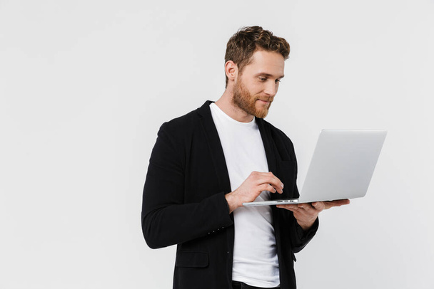Образ красивого задоволеного чоловіка в куртці посміхається і використовує ноутбук ізольовано на білому тлі
 - Фото, зображення