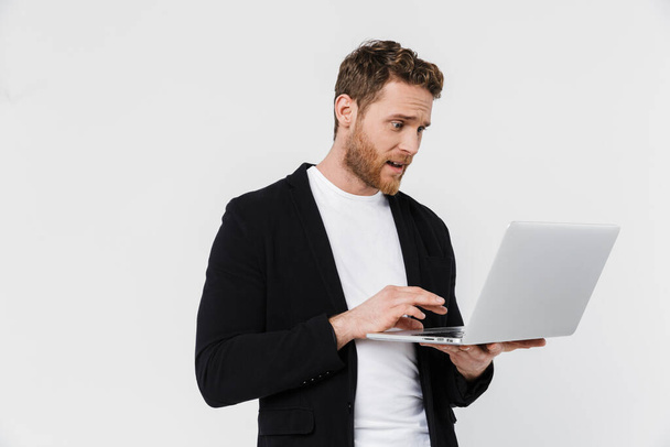 Image of handsome surprised man in jacket holding and using laptop isolated over white background - Фото, зображення