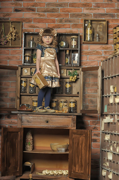little girl in a dress and apron plays in a vintage kitchen - 写真・画像
