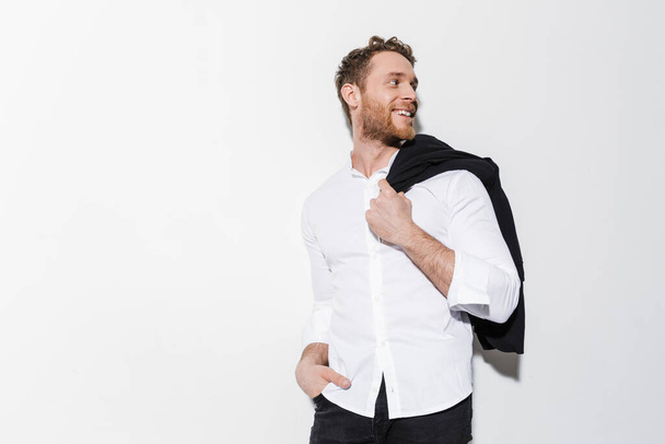 Image of handsome joyful man in shirt holding black jacket and smiling isolated over white background - 写真・画像