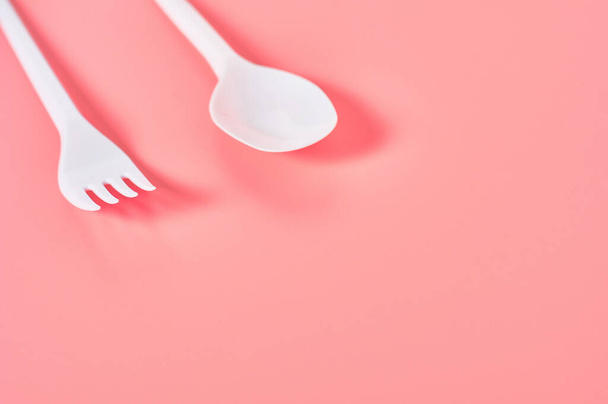 White disposable spoon and fork on pink background. Concept of save environment, ecology, recreation on picnic, party and other events. Copy space - Photo, image