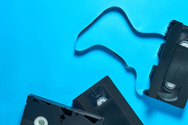 Rozrzucone wiele czarnych starych plastikowych kaset wideo vhs leży na niebieskim biurku. Koncepcja lat 90. Odbiór. Widok z góry - Zdjęcie, obraz