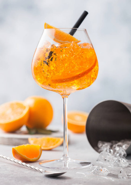 Glass of aperol spritz summer cocktail with oranges and bar spoon and cocktail shaker on light table background. Ice cubes and black straw. - Foto, imagen