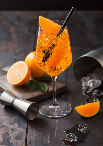 Glass of aperol spritz summer cocktail with oranges and bar spoon with cocktail shaker on wooden background with ice cubes. - Photo, Image