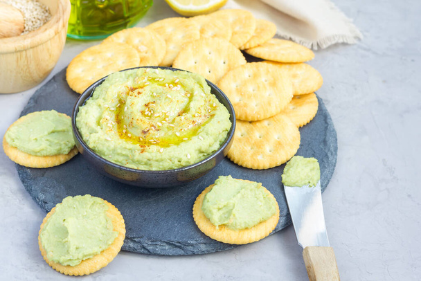 Healthy avocado hummus sprinkled with olive oil, paprika and sesame, served with crackers, horizontal, copy space - Fotó, kép