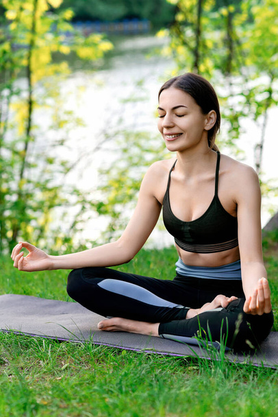 młoda dziewczyna na świeżym powietrzu w lecie na macie do jogi siedzi w pozycji lotosu - Zdjęcie, obraz