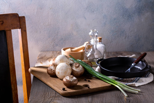 Products for the preparation of mushroom dishes. Champignons, green onions on a wooden table. Cooking concept. - 写真・画像