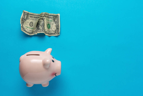 Piggy bank with a crumpled dollar bancnote on blue background . Minimal Coronavirus outbreak. Saving money concept. - Foto, immagini