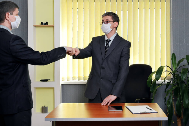 スーツ姿の男と医療面の男がテーブルから立ち上がり、事務所に来た人に挨拶をした。伝染病の脅威に対する伝統的な握手を捨て - 写真・画像