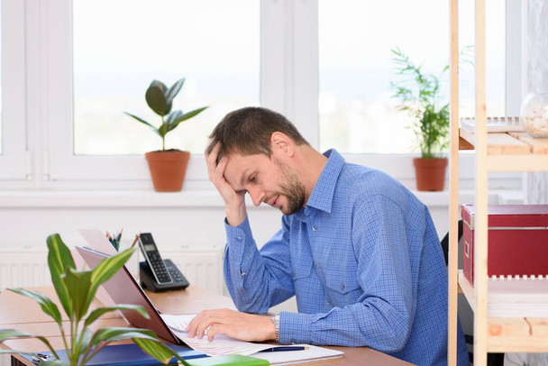 Upset office worker looking at documents clutching his head - Photo, Image