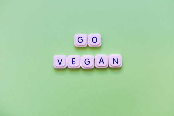 Go vegan μήνυμα φτιαγμένο από μπλοκ επιστολή παιχνίδι πάνω από ένα φωτεινό πράσινο φόντο. Μήνυμα που ενθαρρύνει τους ανθρώπους να γίνουν χορτοφάγοι - Φωτογραφία, εικόνα