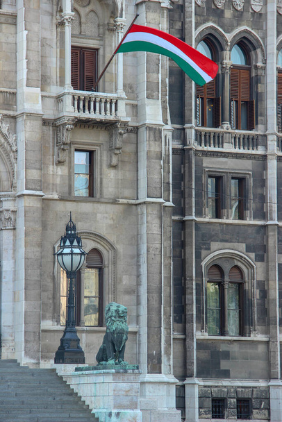 Budapest, Hungary - May 11, 2012: Facade of the Hungarian Parliament Building with the statue of a guarding lion next to a lamppost and a flag waving above. - Fotó, kép