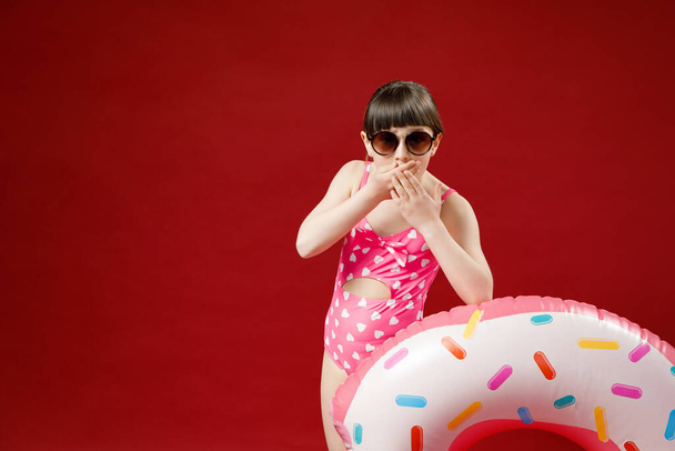 Isolated shot of charming little girl in sunglasses posing in studio with rubber ring going to have swim in sea during vacations. Pretty female child holding swimming inflatable circle - Fotoğraf, Görsel