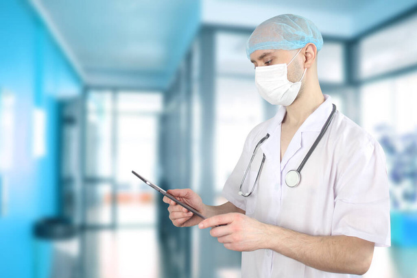 mladý muž, lékař, lékárník v bílé uniformě a maska drží v ruce tablet, koncept gadgets, moderní technologie v medicíně, léčba nemocí, coronavirus, COVID-19 - Fotografie, Obrázek