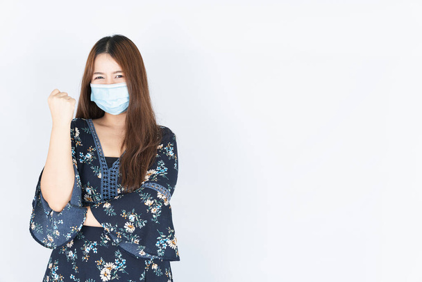 Asian beautiful happy hipster woman wearing a medical protection face mask for protect the coronavirus, filter dust PM 2.5 and cold and raise her hand to fight them on white background - Photo, Image