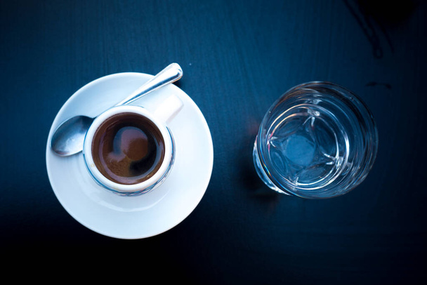 Geleneksel İtalyan usulü bir bardak suyla servis edilen kahve. Üst Manzara. Barda sabah kahvesi. Espresso geometrik konsept. Kahve çılgınlığı, siyah ve beyaz. Bir fincan sıcak içecekle izole edilmiş. - Fotoğraf, Görsel