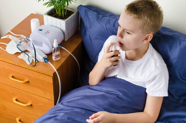 Beteg fiú lélegzik az inhalátor maszkon keresztül. Használata porlasztó és inhalátor kezelésére vagy légúti betegségek megelőzésére, mint például a koronavírus, asztma és allergia. Otthoni terápia. - Fotó, kép