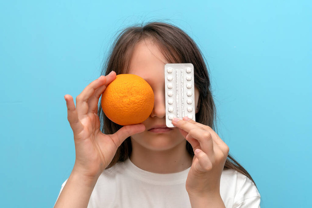 Una bambina di 10 anni tiene in mano una pillola arancione e una di allergia. La faccia è chiusa. Allergia al cibo e agli agrumi
 - Foto, immagini