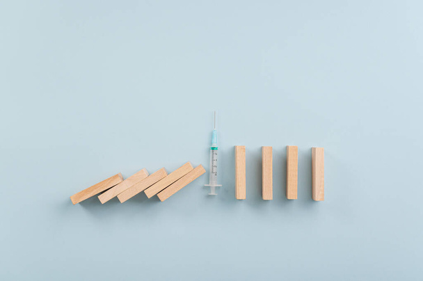 Disease prevention conceptual image - medical injection in the middle of collapsing dominos to prevent the spread of an infectious virus. - Фото, изображение