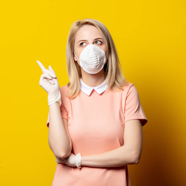 Blonde girl in face mask and pink dress on yellow background. - Photo, Image