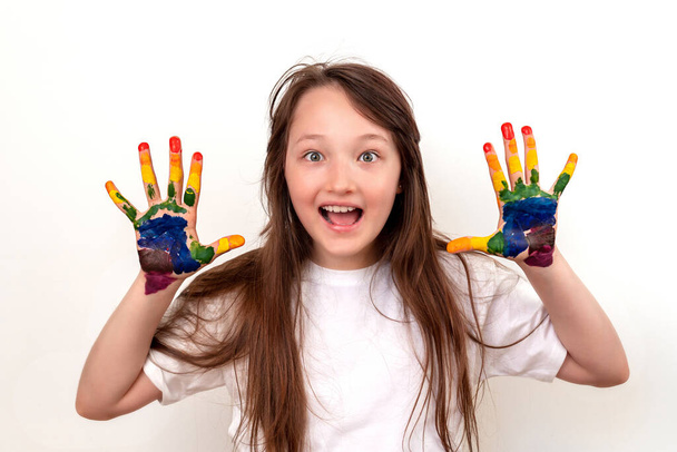 Porträt eines glücklichen und lächelnden Mädchens mit bunten Handflächen. Das Mädchen sieht überrascht und begeistert aus, die Augen weit aufgerissen. Regenbogen auf den Händen. Farbige Hände - Foto, Bild