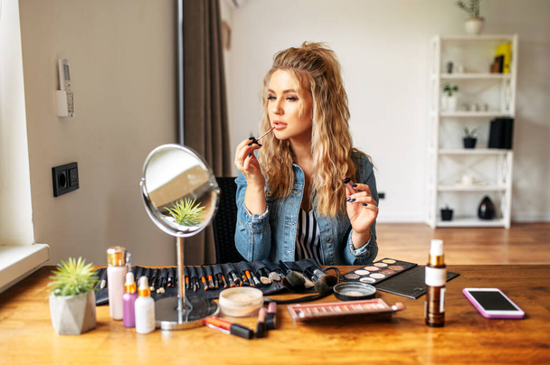 Young woman looks at mirror and doing makeup - Foto, afbeelding