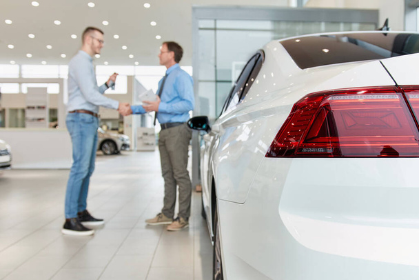 Stringere la mano dopo un acquisto di auto di successo in showroom auto moderne. Concentrarsi sul veicolo
. - Foto, immagini