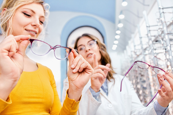 Optician suggesting and showing eyeglasses in an optical shop, finding the right frame for prescription glasses - Photo, Image