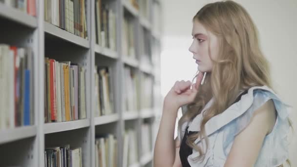 Junge attraktive blonde Studentin nimmt zwei Bücher aus dem Regal in der Bibliothek - Filmmaterial, Video