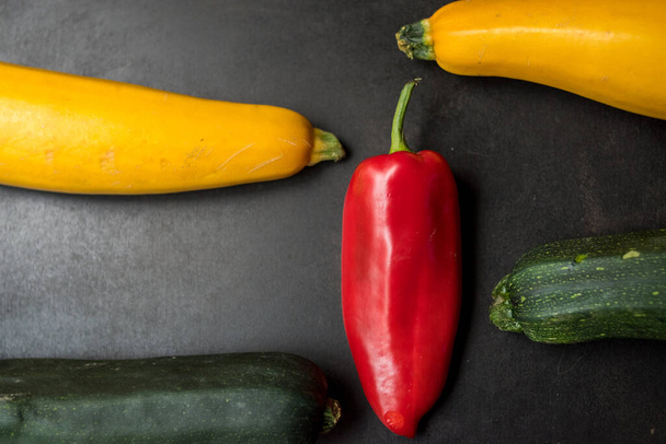 Big red pepper surrounded by some green and yellow vegetables on a wooden surface - Foto, Imagen