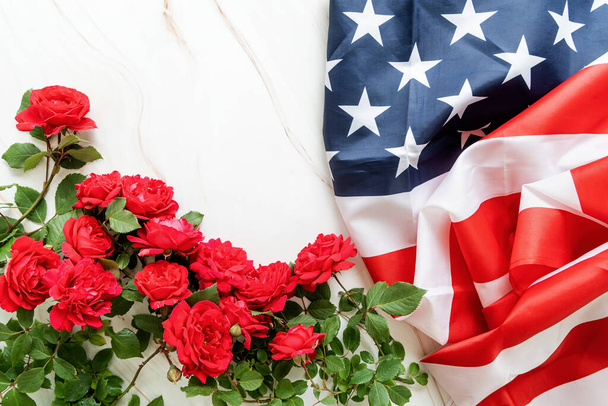 Independence Day USA concept. Memorial Day. Red roses over the USA flag top view flat lay with copy space - Foto, imagen
