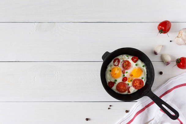 Fresh delicious breakfast of eggs and tomatoes with spices and red pepper, frying pan with fried eggs on white wooden background, top view, copy space - Photo, Image
