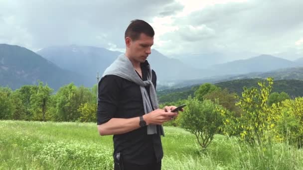 bel homme en vêtements décontractés en utilisant smartphone pendant la promenade dans les montagnes le jour d'été - Séquence, vidéo