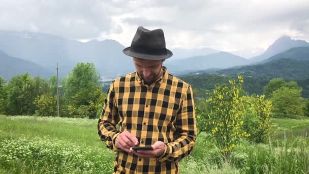 komea mies rento vaatteita älypuhelimella kävelyn aikana vuorilla kesäpäivänä - Materiaali, video